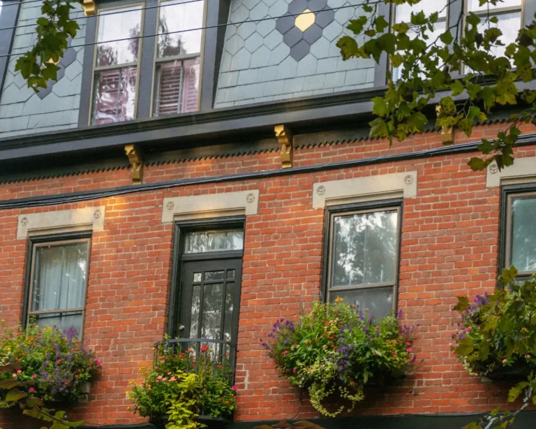 Three-storey red brick rowhouse facade with stone window heads, a dark front door and window boxes full of flowers