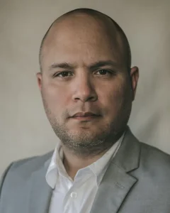 Tomas, a man in a grey blazer and open white shirt, looking straight at the camera
