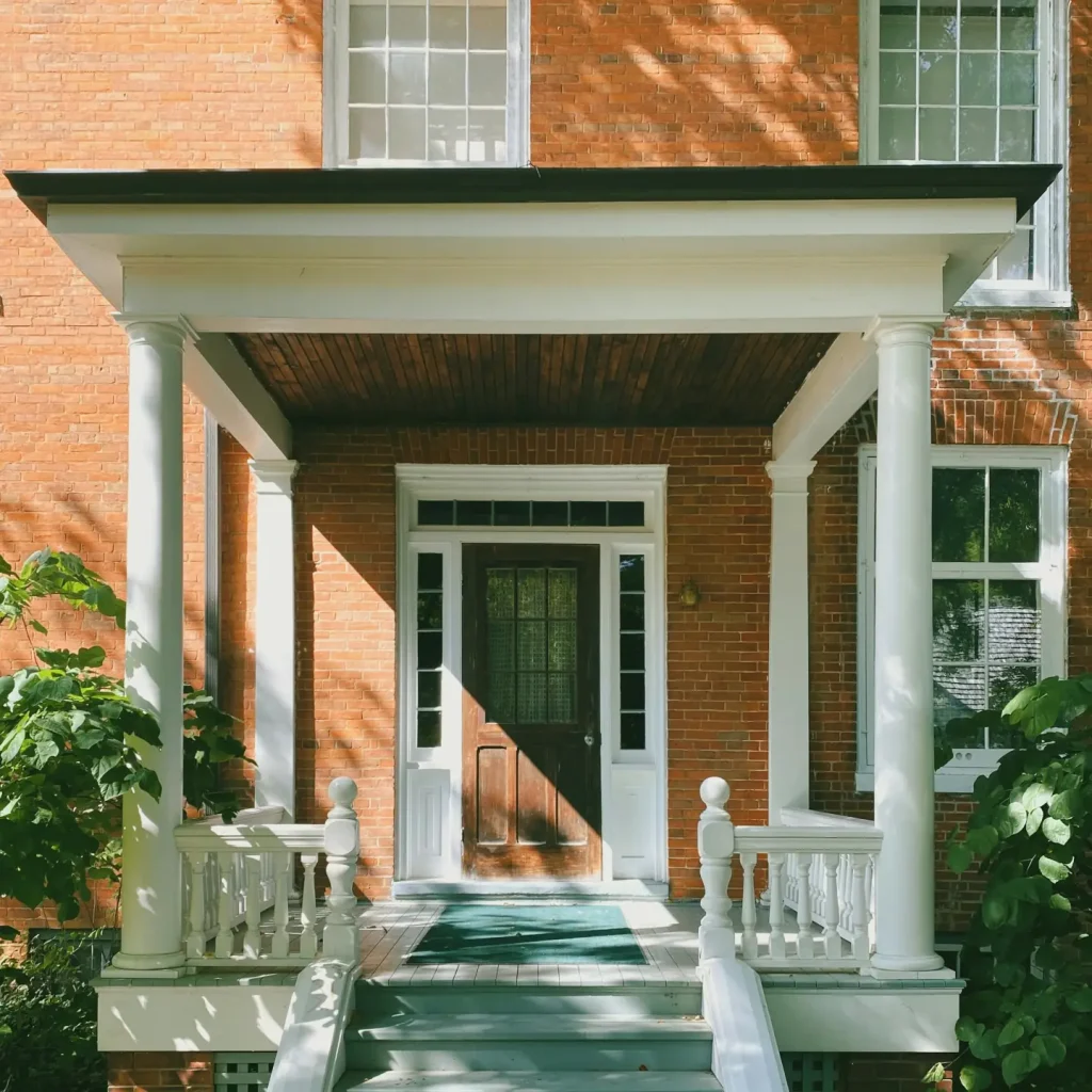 White columned porch and green painted steps leading to a dark front door on a red brick house